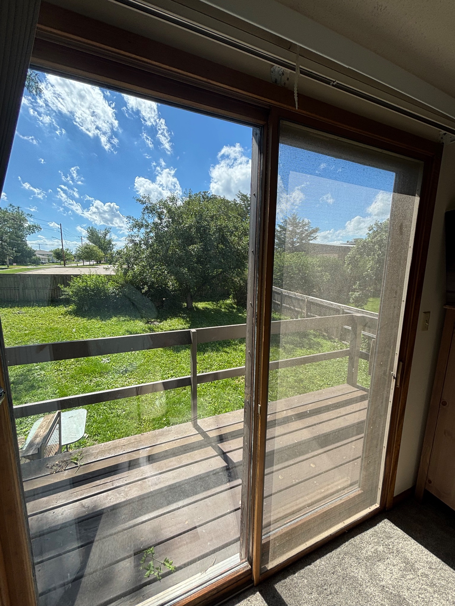 Before photo of an old sliding patio door in Ames, showing a weathered wooden frame and screen, looking out onto a deck and green backyard.