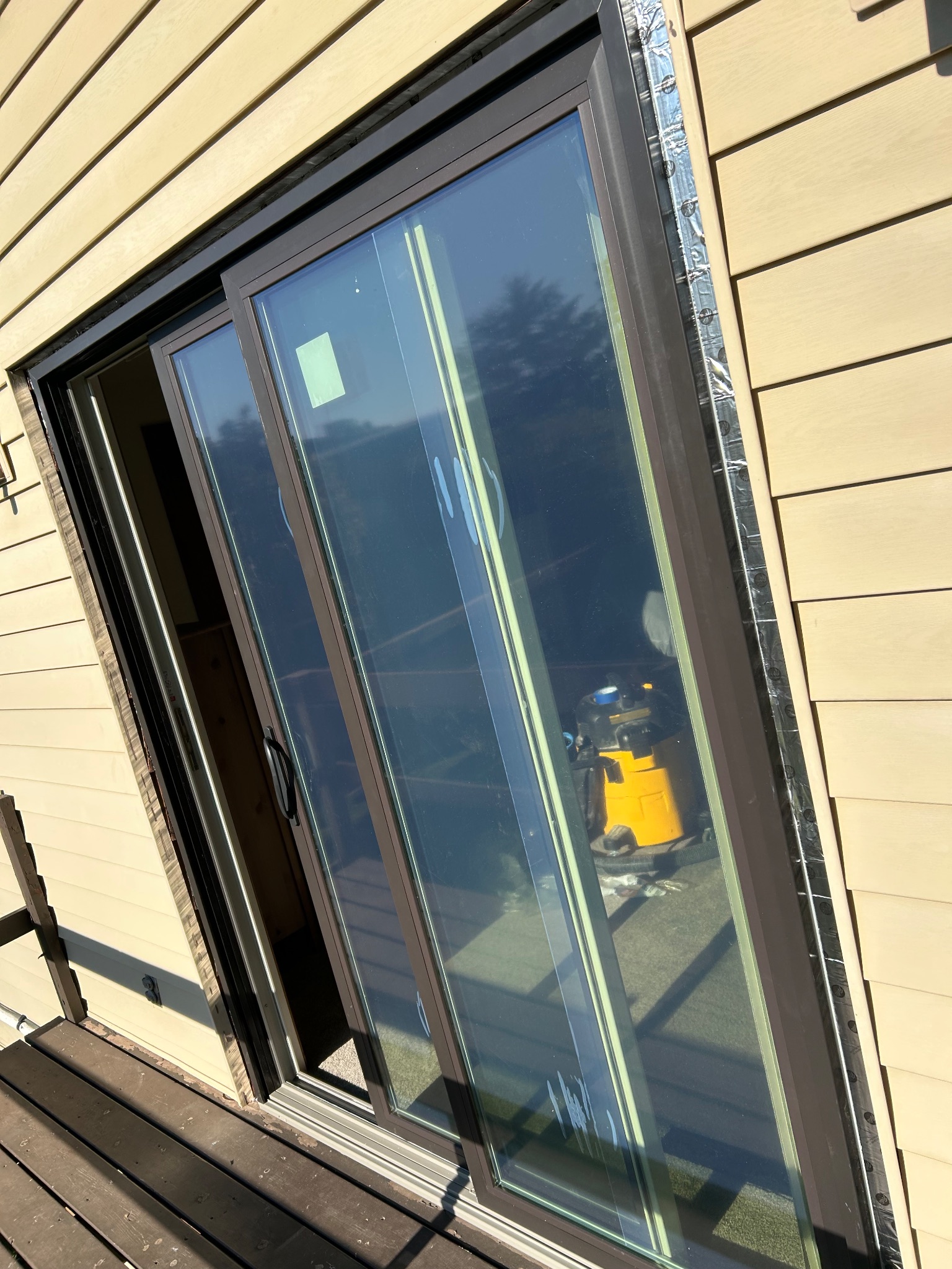 After photo of a newly installed brown vinyl sliding patio door in Ames, with fresh flashing visible along the exterior siding, reflecting a clear sky.