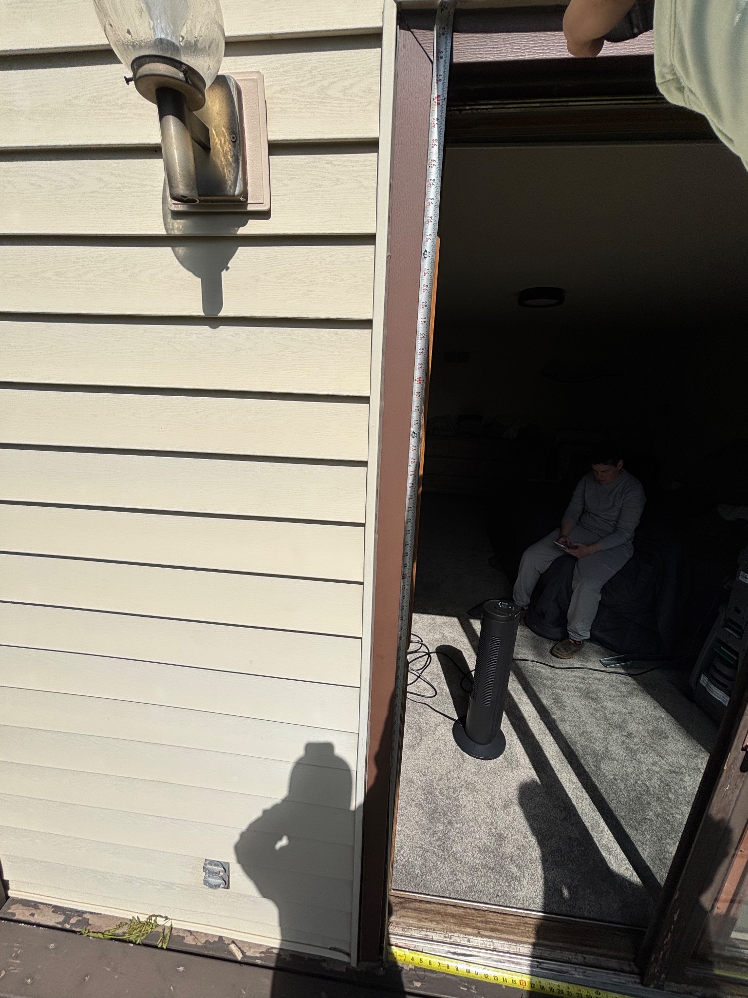 A team member taking a vertical measurement of the patio door opening from the exterior in Ames, showing the house siding and an old light fixture.
