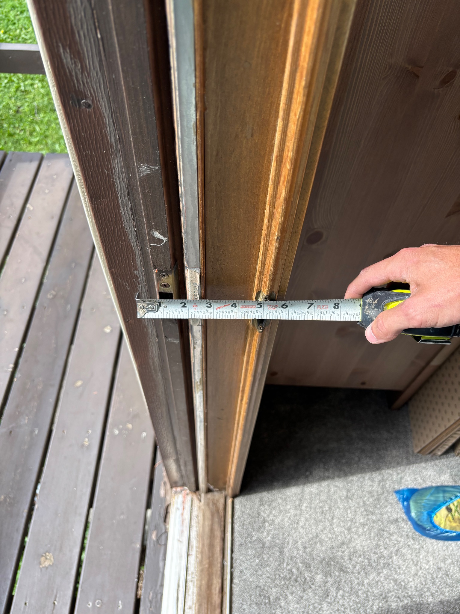 A hand holding a tape measure against the existing door frame, indicating its width, as part of the patio door replacement preparation in Ames.