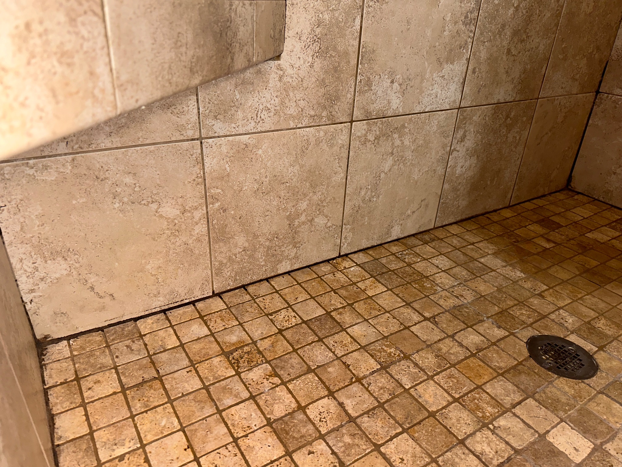 Before photo of a tiled shower floor and wall junction with dark, mildewed caulk in Johnston, Iowa, as part of a shower grout and caulk remediation project.