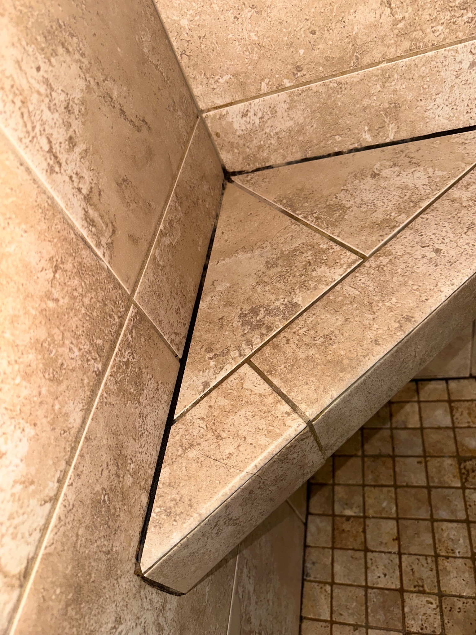 After photo of a tiled shower bench with clean, new caulk in the corner in Johnston, Iowa, after a shower grout and caulk remediation project.