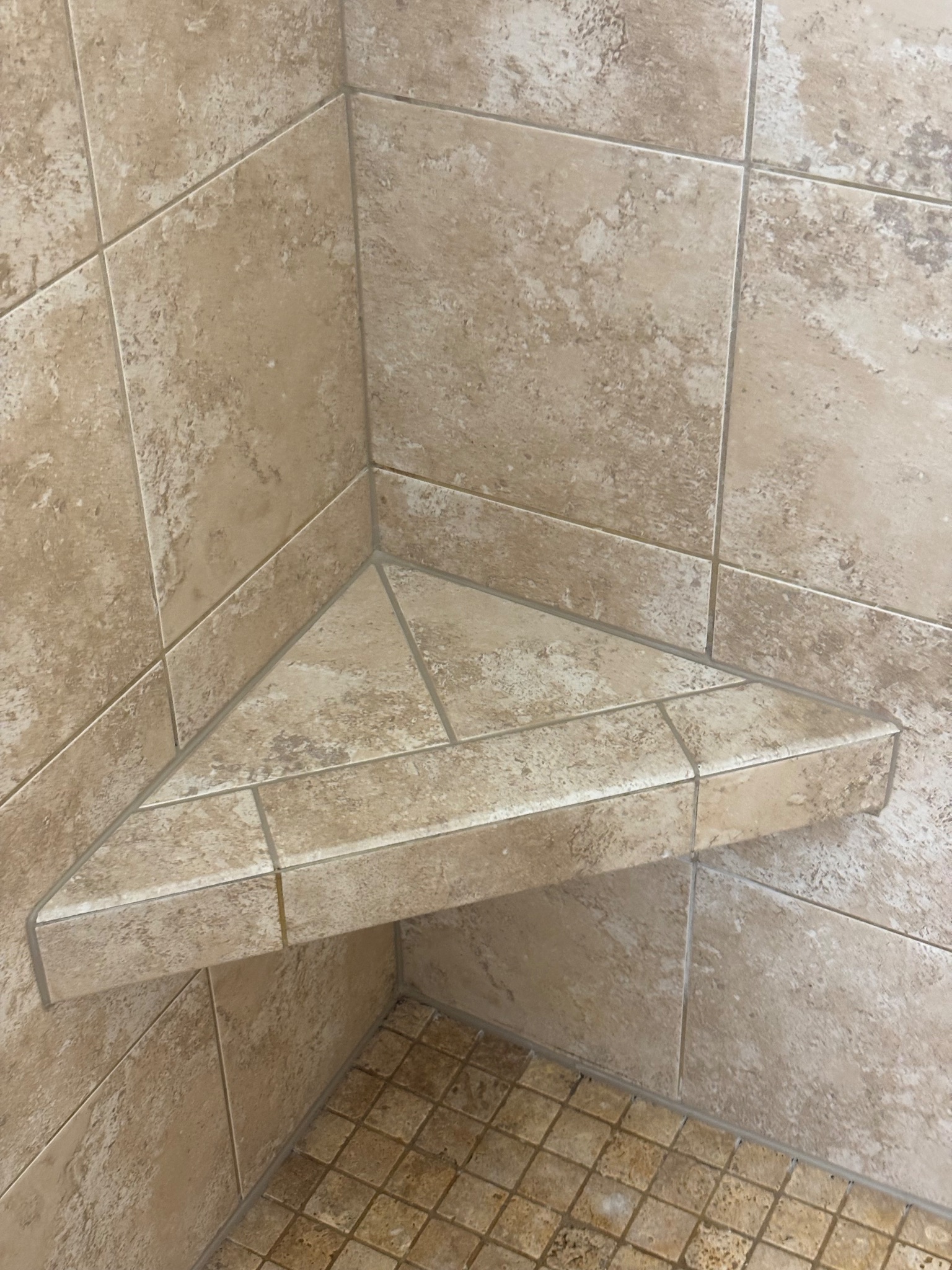 Detail photo of a clean tiled shower bench corner with fresh caulk in Johnston, Iowa, after a shower grout and caulk remediation project.