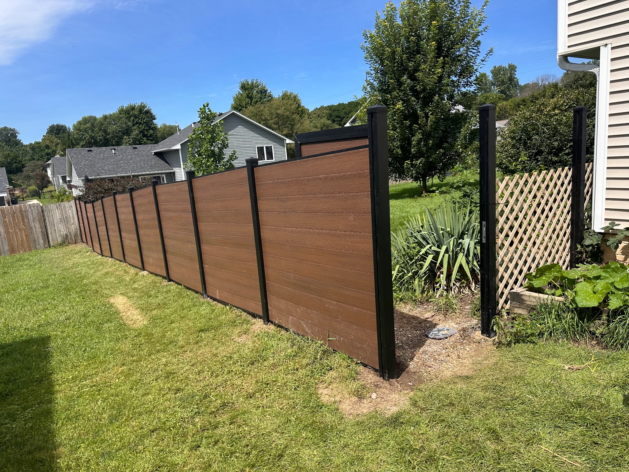 Side view of a newly installed brown composite fence with a temporary lattice section in Des Moines, Iowa