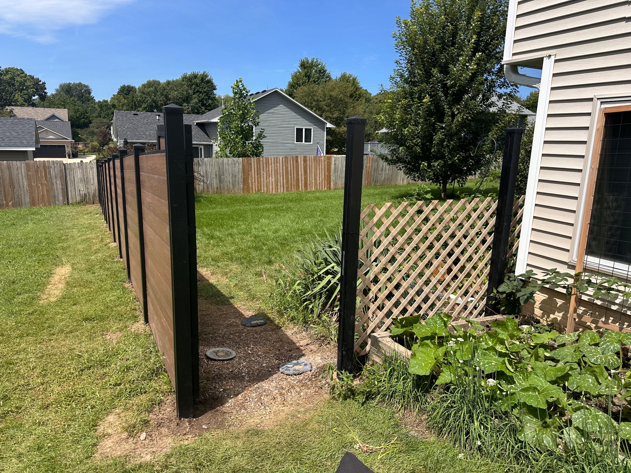 Backyard view of a new brown composite fence alongside existing landscaping in Des Moines, Iowa