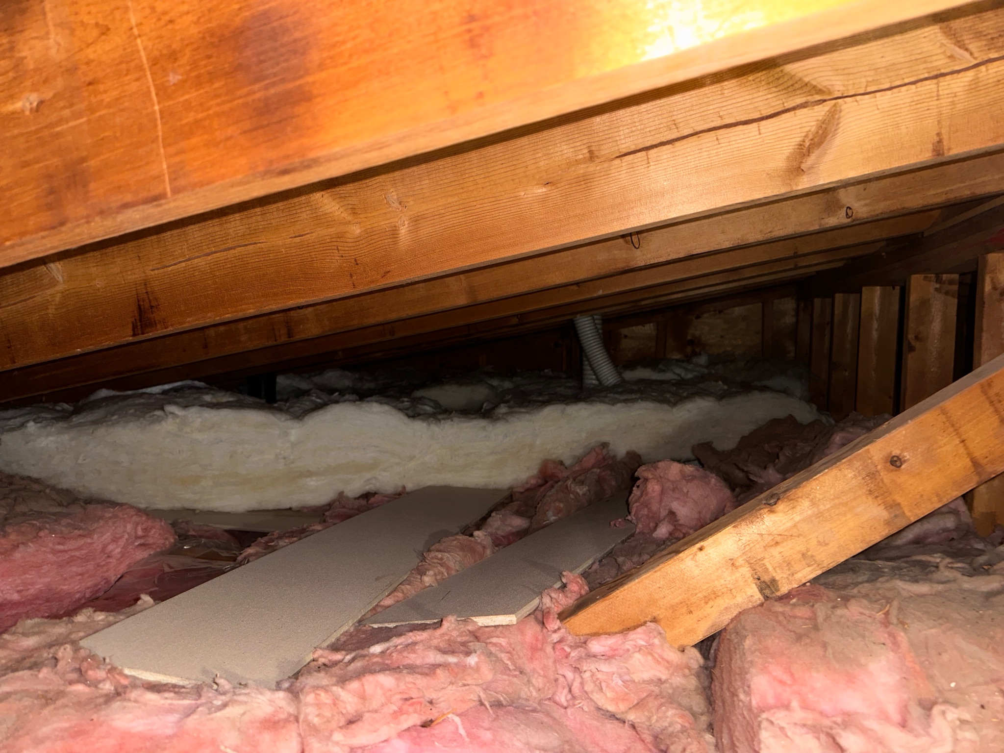 Attic space with existing pink and white batt insulation and exposed wooden rafters in Ames, Iowa, before insulation upgrade.