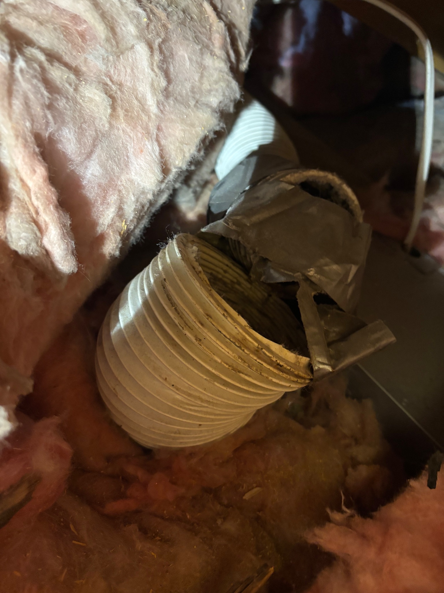 Damaged and poorly taped bath fan vent line in an attic in Ames, Iowa, before repair.