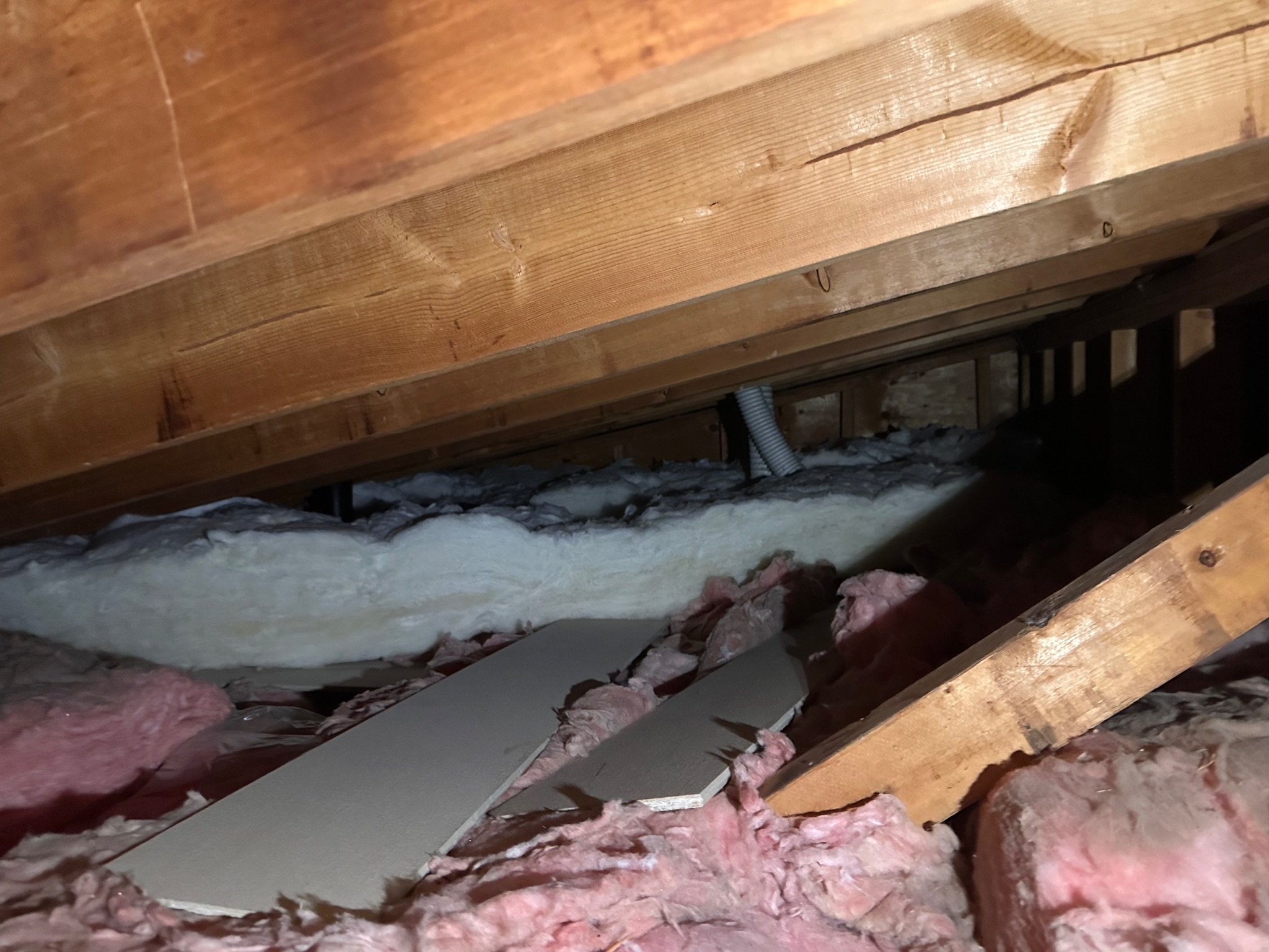 Attic space with existing insulation and exposed wooden rafters in Ames, Iowa, before insulation upgrade.