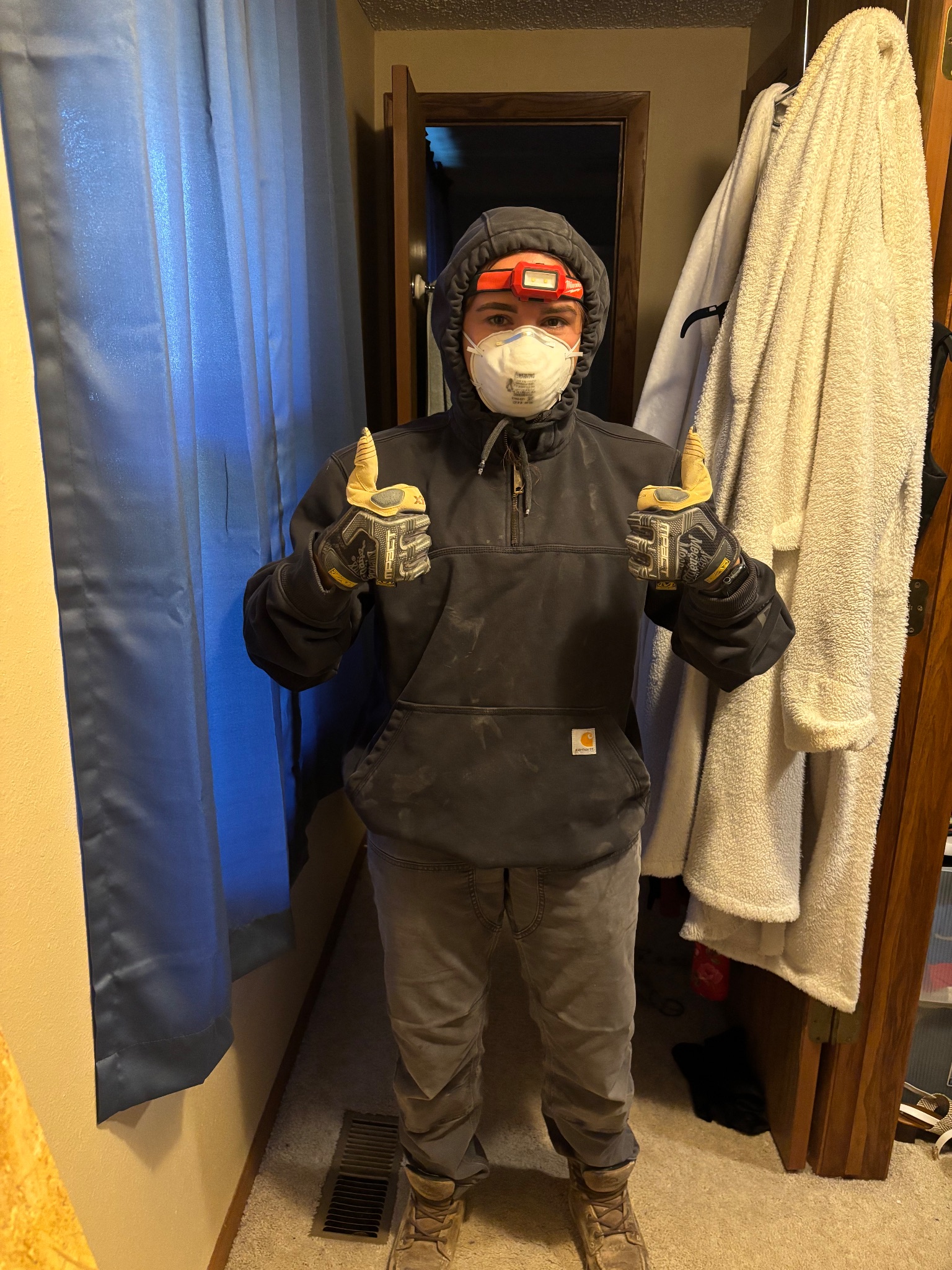Co-Owner Whitney in protective gear and headlamp giving a thumbs up in Ames, Iowa, during an attic insulation project.