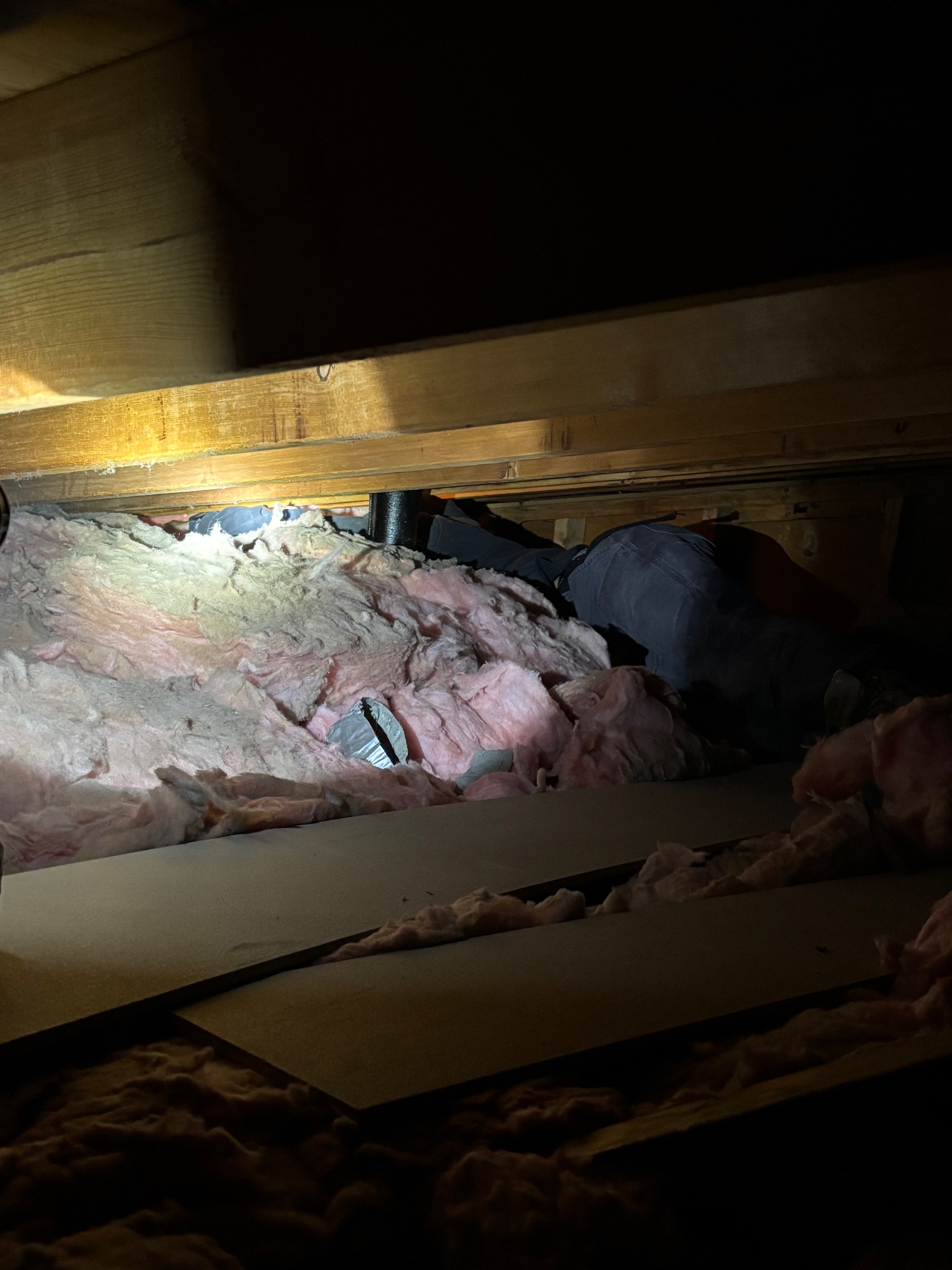 Handyman working in an attic, installing batt insulation around a bath fan vent line in Ames, Iowa.