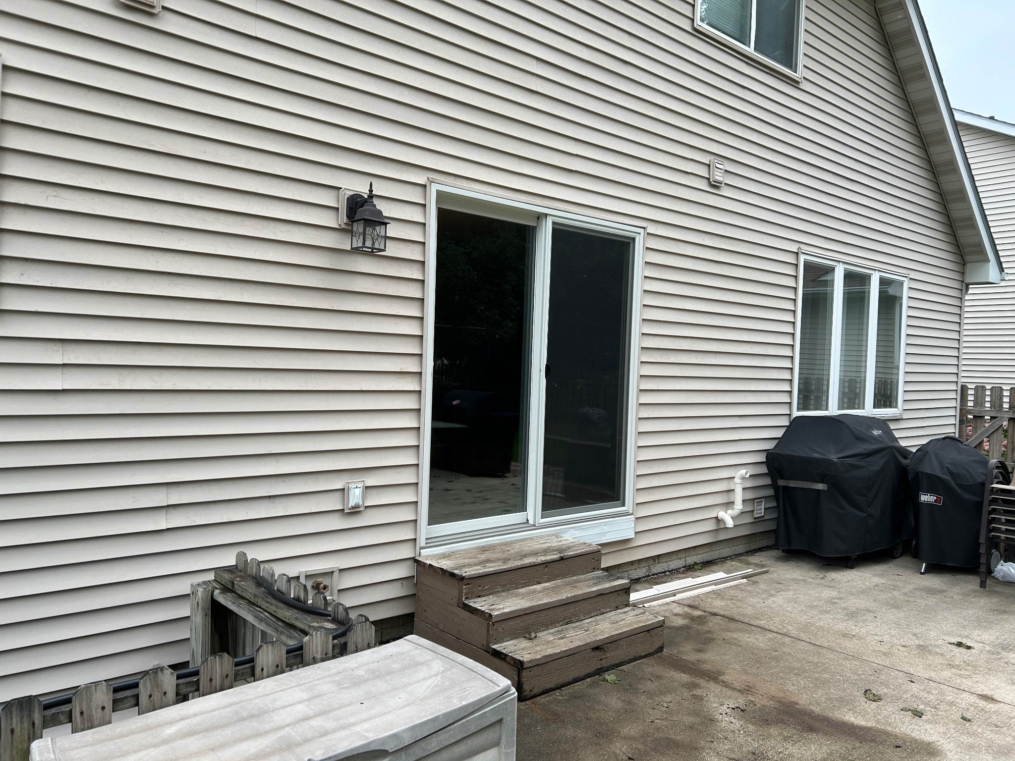 Before image of an old beige siding house in Ames with a worn sliding patio door, wooden steps, and a concrete patio.