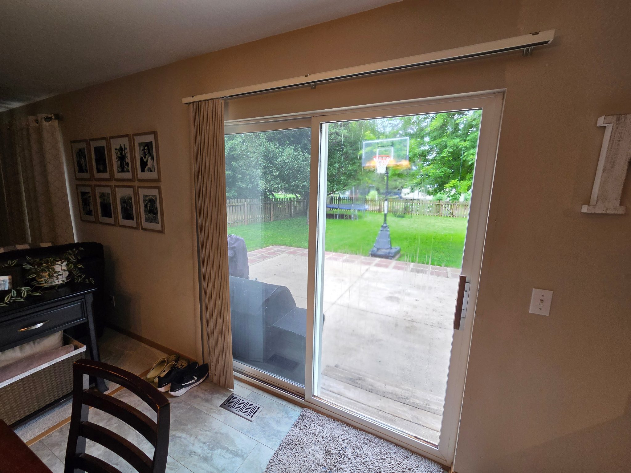 After image of a new white vinyl sliding patio door with a screen, viewed from the inside of a home in Ames, looking out to a backyard.