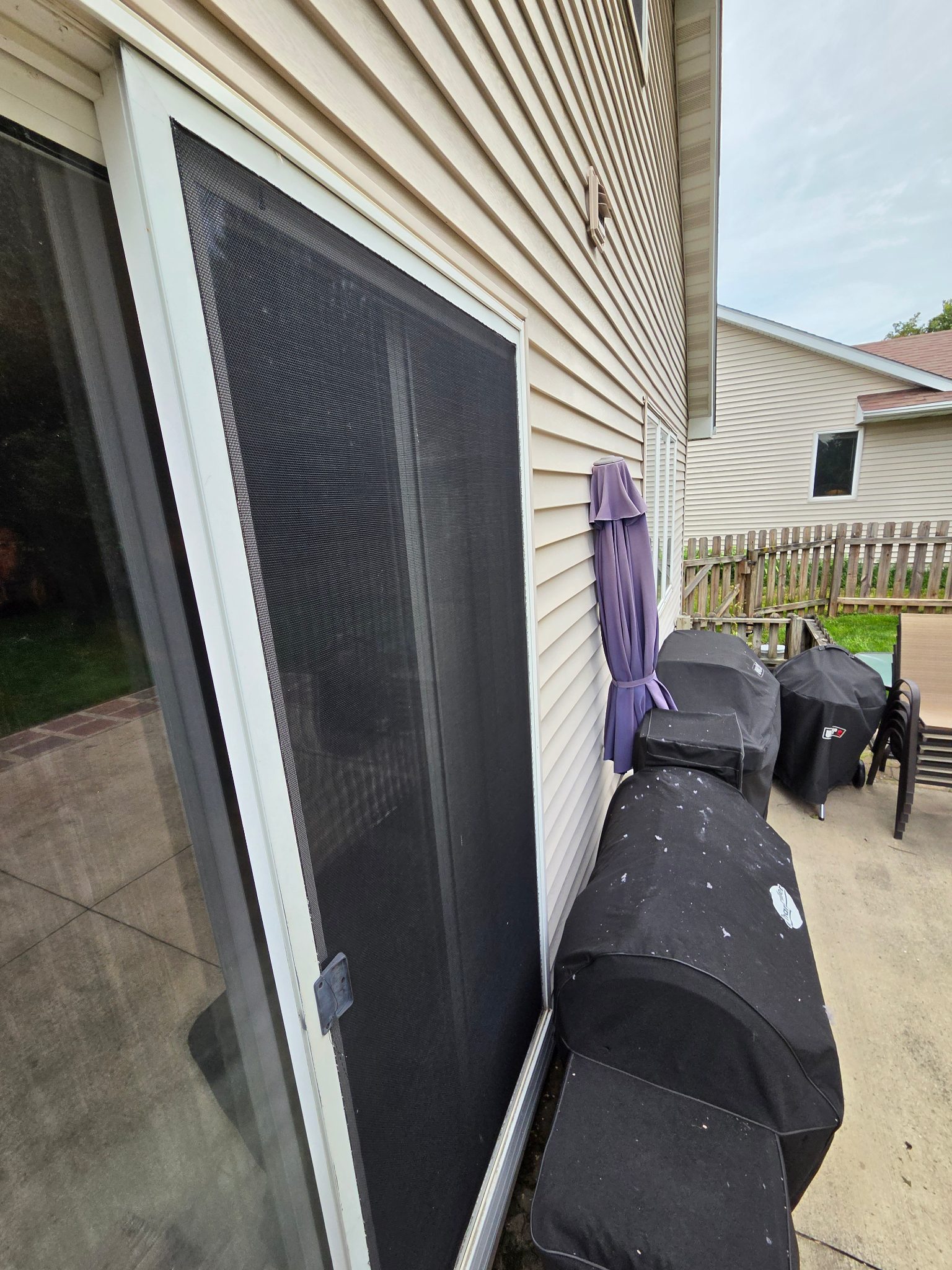 Detail image of the exterior of a new white vinyl sliding patio door with a screen in Ames, next to barbecue grills.