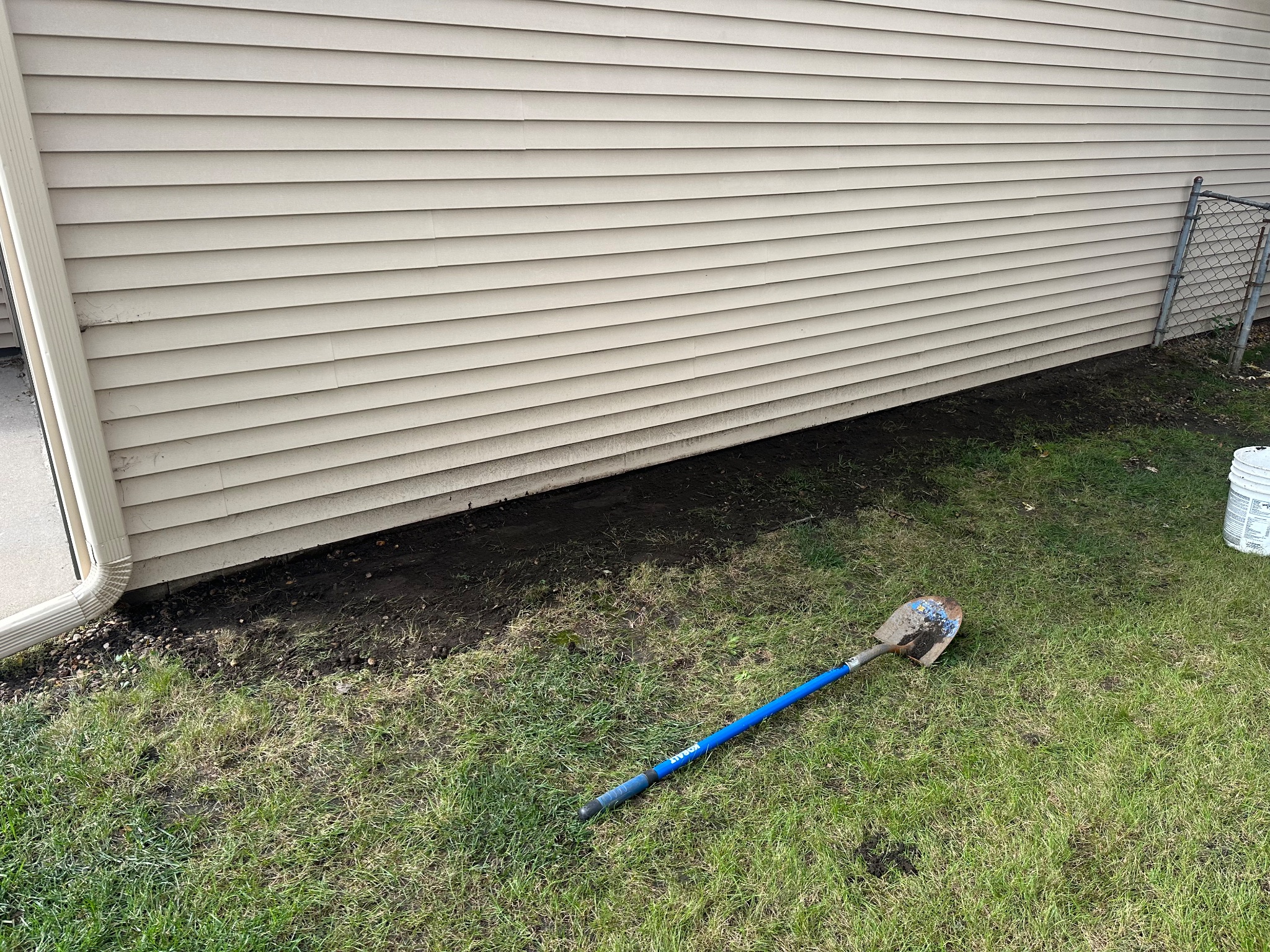 Regraded area alongside house with shovel and clear space under siding in Ames handyman project.