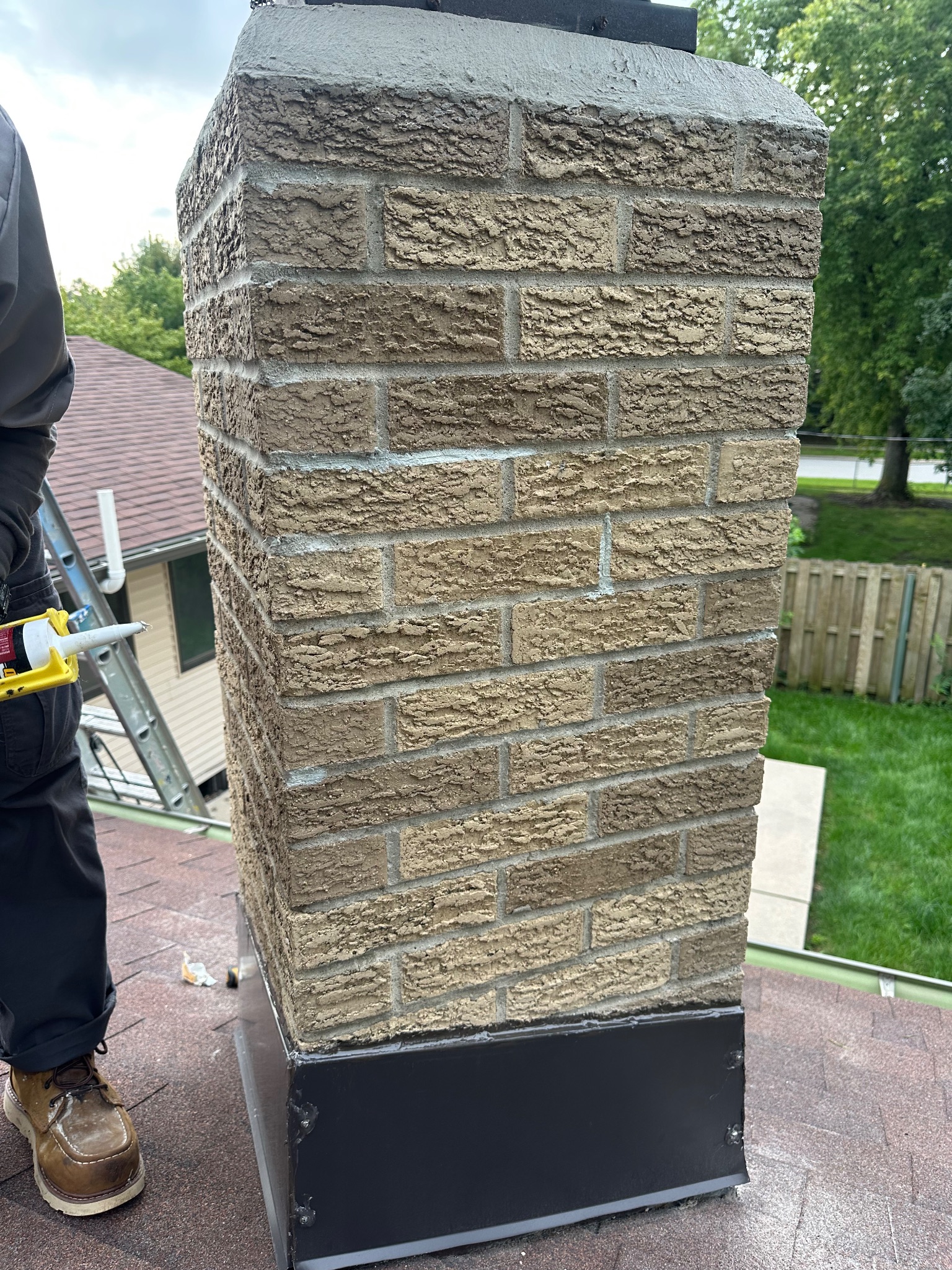 Technician applying sealant to chimney flashing on a roof in Ames handyman project.