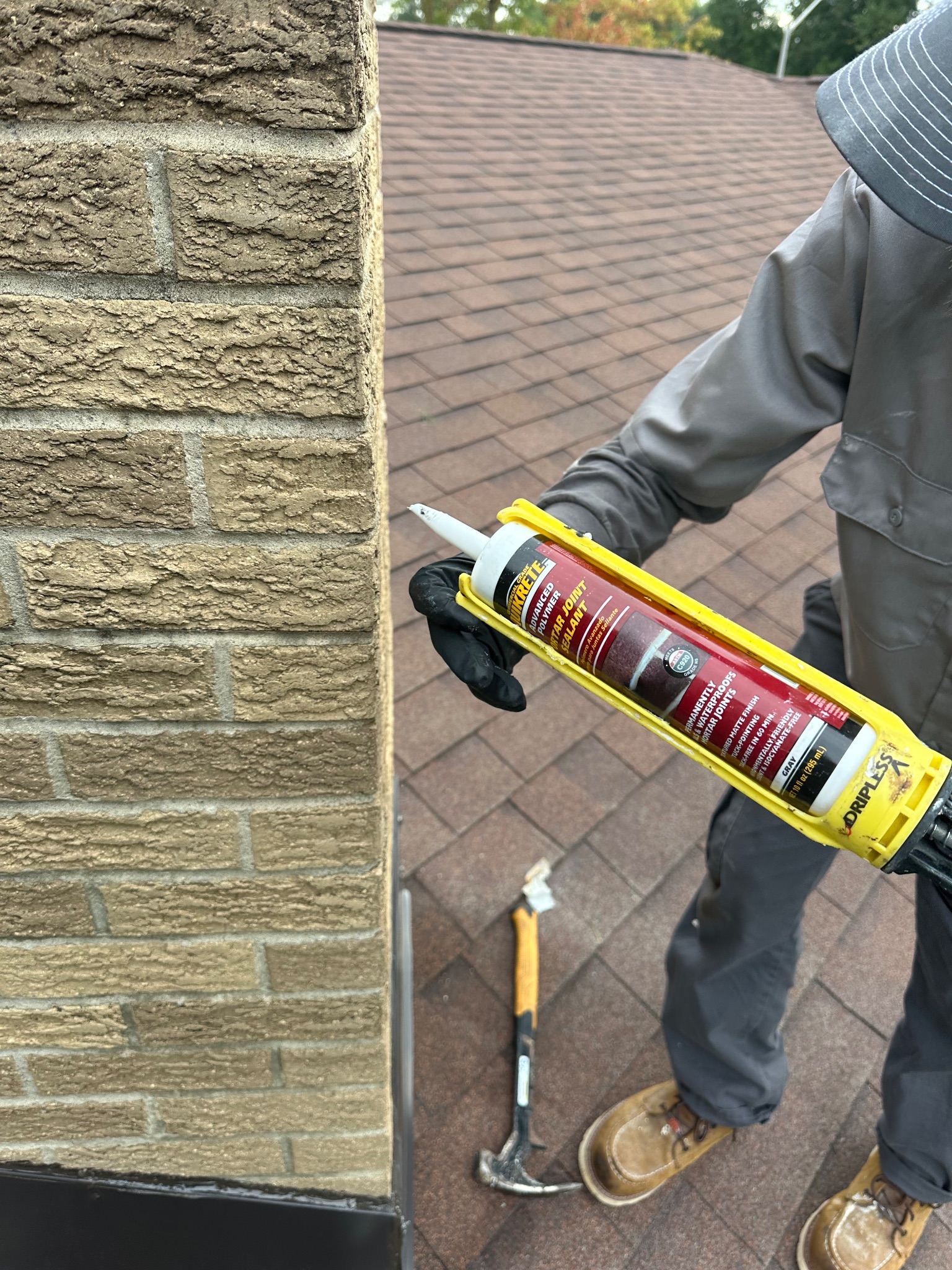 Technician holding a caulk gun near a chimney on a roof in Ames handyman project.